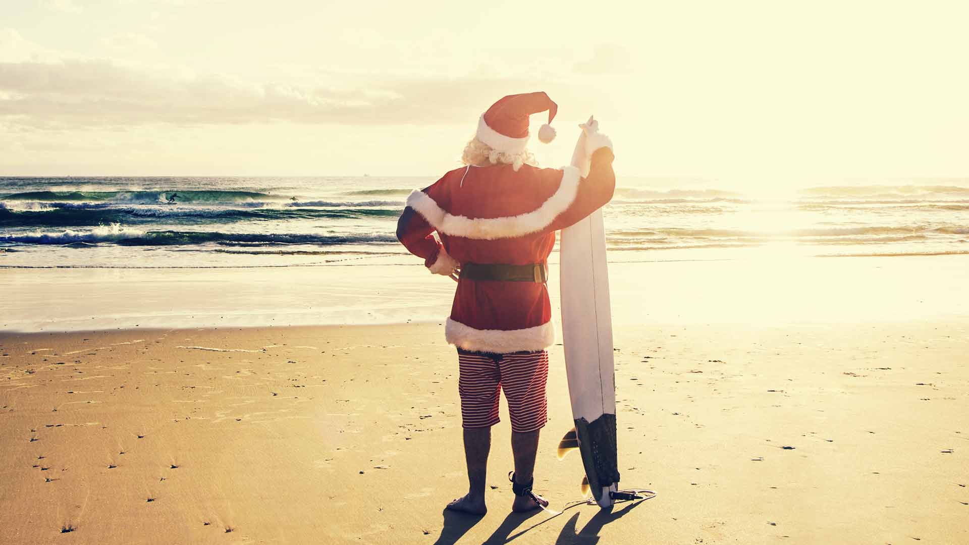 Man in a Santa Claus standing on the beach in the sunshine.
