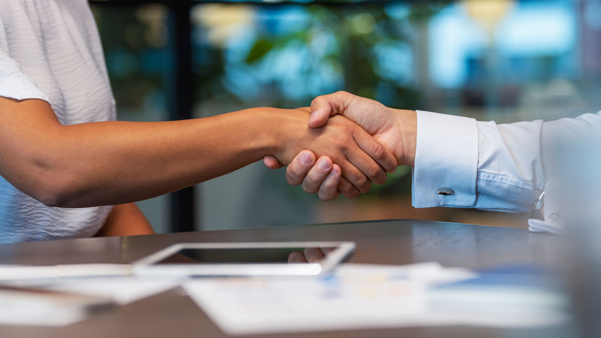 Image of business people shaking hands over a desk in an office.
