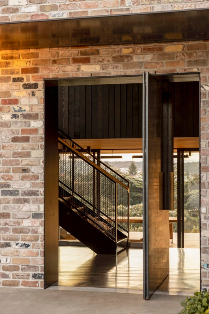 A rusted steel door opening to a staircase with floor-to-ceiling windows in the background.