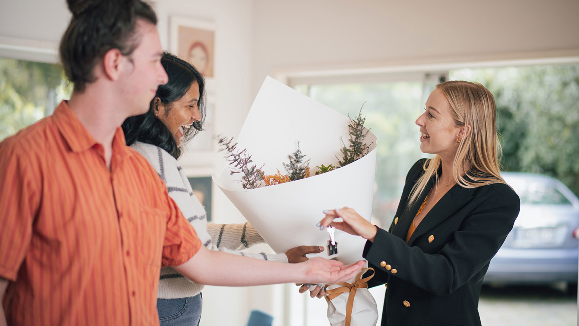 Real estate agent handing over flowers and keys to a couple that have just bought a house in New Zealand