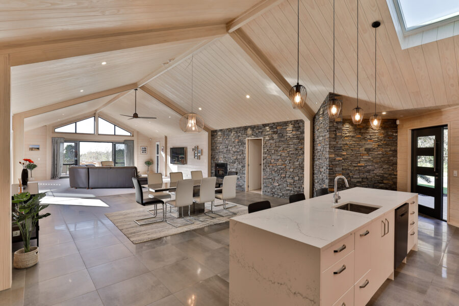 This stunning contemporary Lockwood home in Tauranga features a central schist wall that meets knot-free pine walls. The high sarked ceiling creates a voluminous sense of space and an airy, light open-plan living area. 