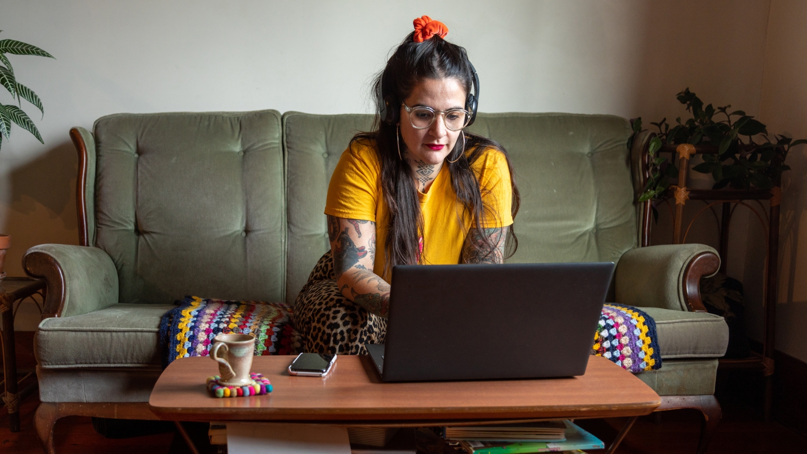 Women in yellow shirt on green couch typing on laptop. 