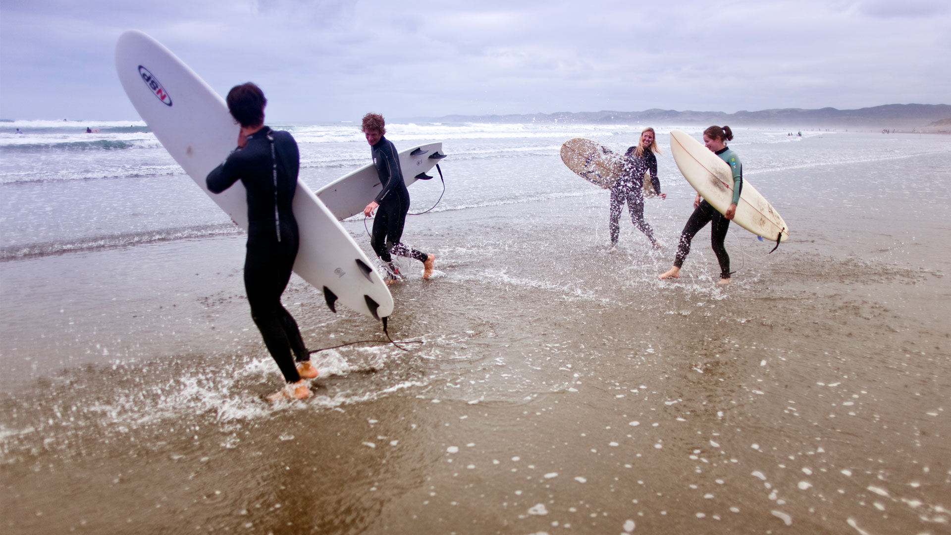 Four surfers heading out into the waves with their boards at Raglan in the Waikato.