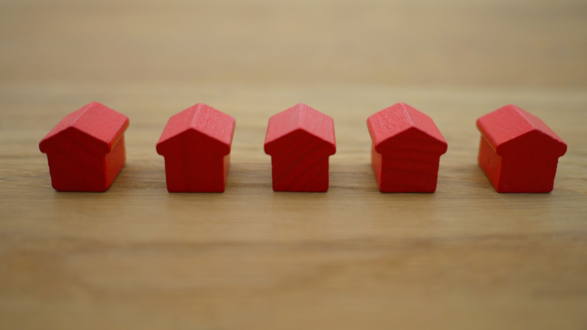 5 red monopoly houses next to each other on a wooden table.