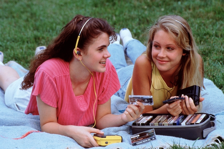 Two young girls lie on a picnic blanket with their cassette tape walkman listening to music