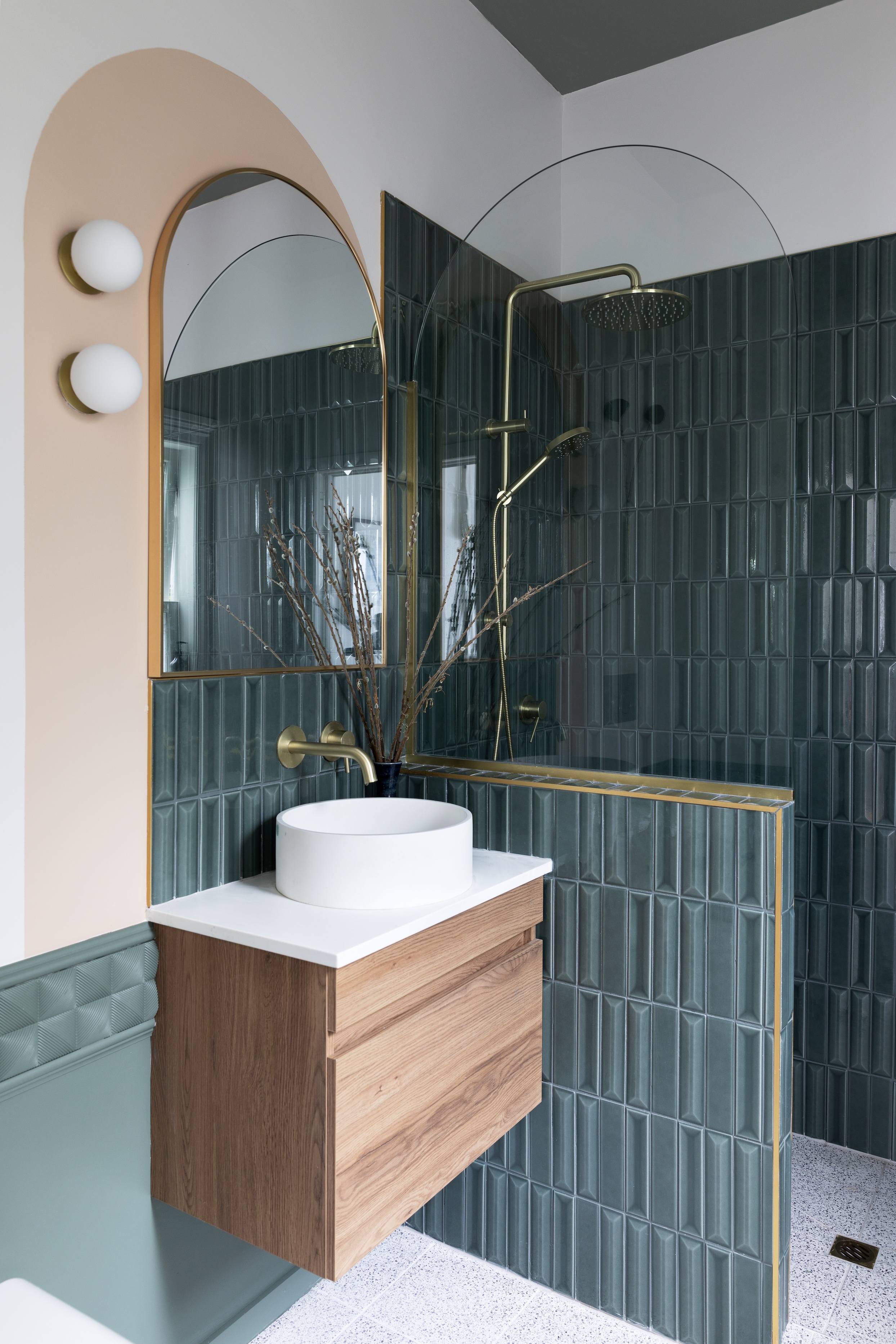 Flauti tiles from Ceramic Vogue beautify the new ensuite, which the couple painted with Resene Ravine on the ceiling, Resene Quarter Tea on the walls and Resene Vantage Point on the decorative panels from Archi Profiles. The pink tones seen elsewhere in the house continue in the asymmetrical arch around the mirror in Resene Cashmere. To create this detail, Gretchen drew around the shower screen to replicate its shape, and waterproofed the back of a mirror from Farmers with Resene Sureseal to get it bathroom-ready beside Artis Opal Globe lights from Lighting Direct.