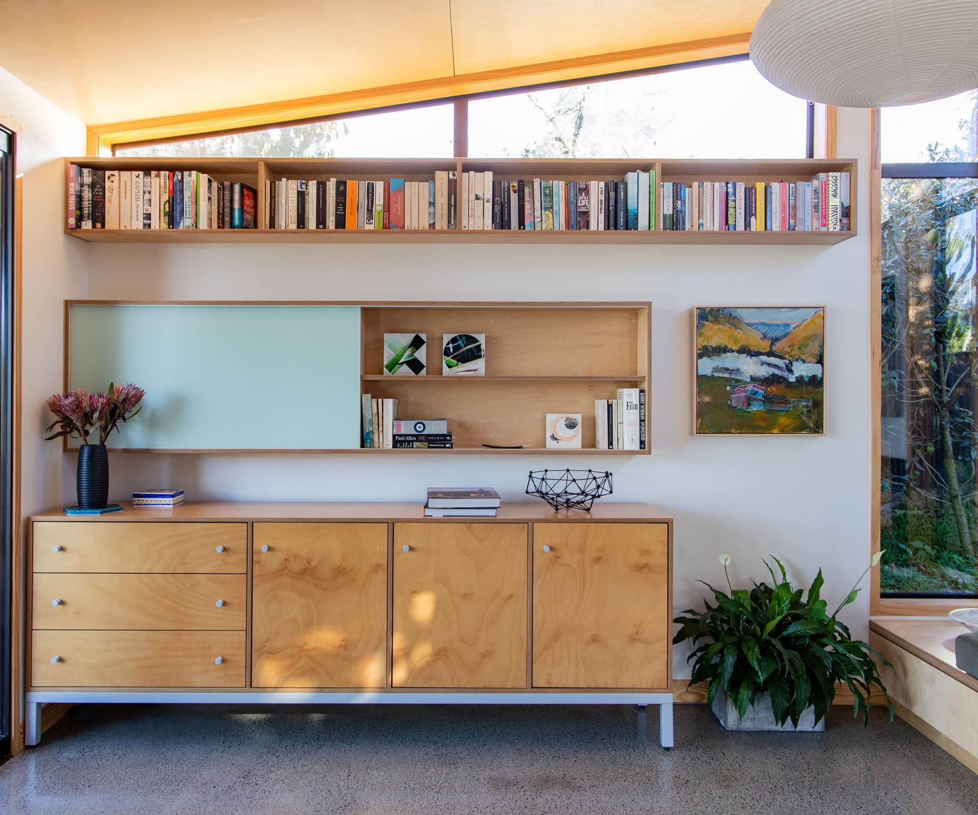 Entryway of the home with a cabinet against the wall, below a built in shelf on the wall that sits below a small floating bookshelf