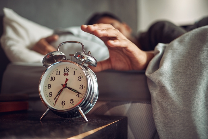 Man reaches out from bed to turn off his vintage alarm clock