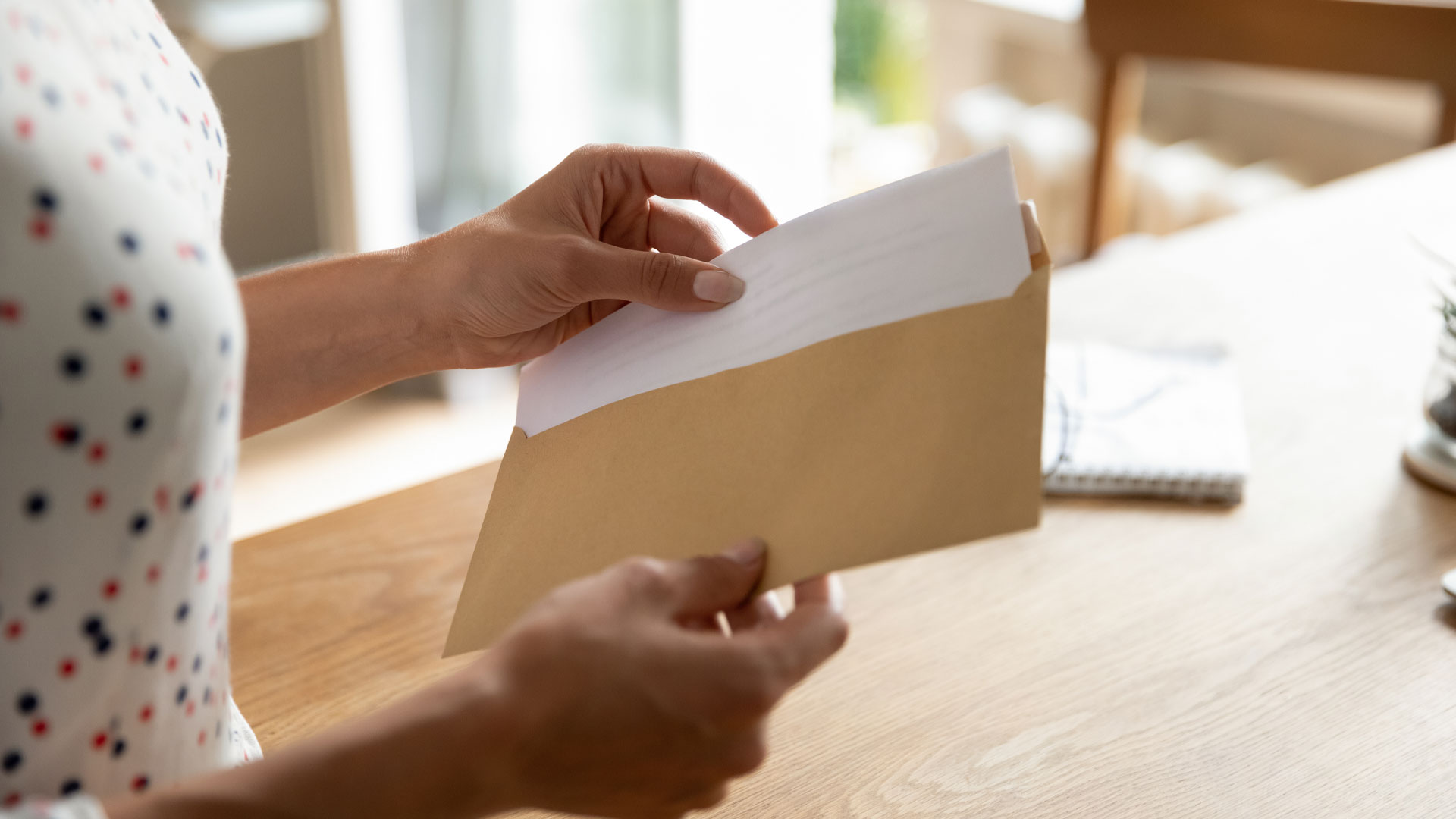 A pair of hands opening a brown envelope containing an offer for a property tender sale.