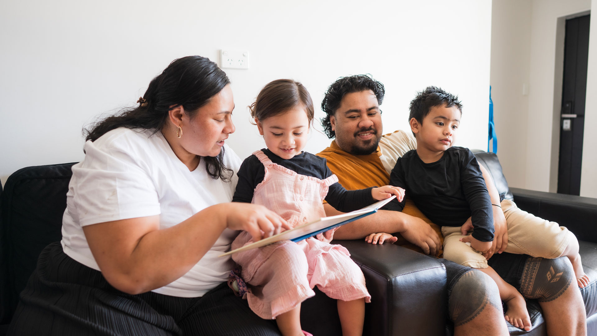 A Māori family at home sitting on the sofa together.