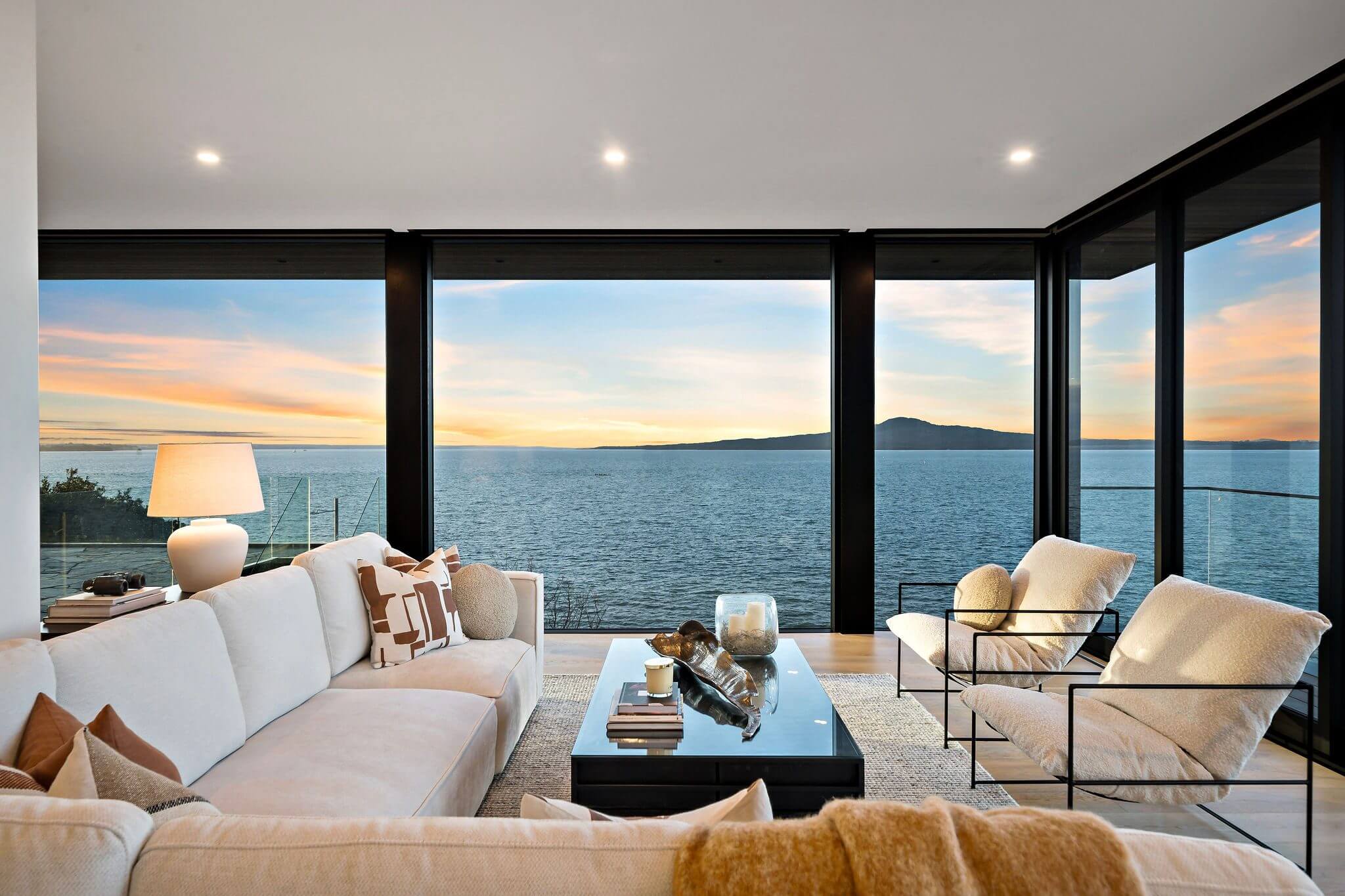 Luxury lounge with cream furnishings, floor-to-ceiling glass walls, and sweeping harbour views at golden hour