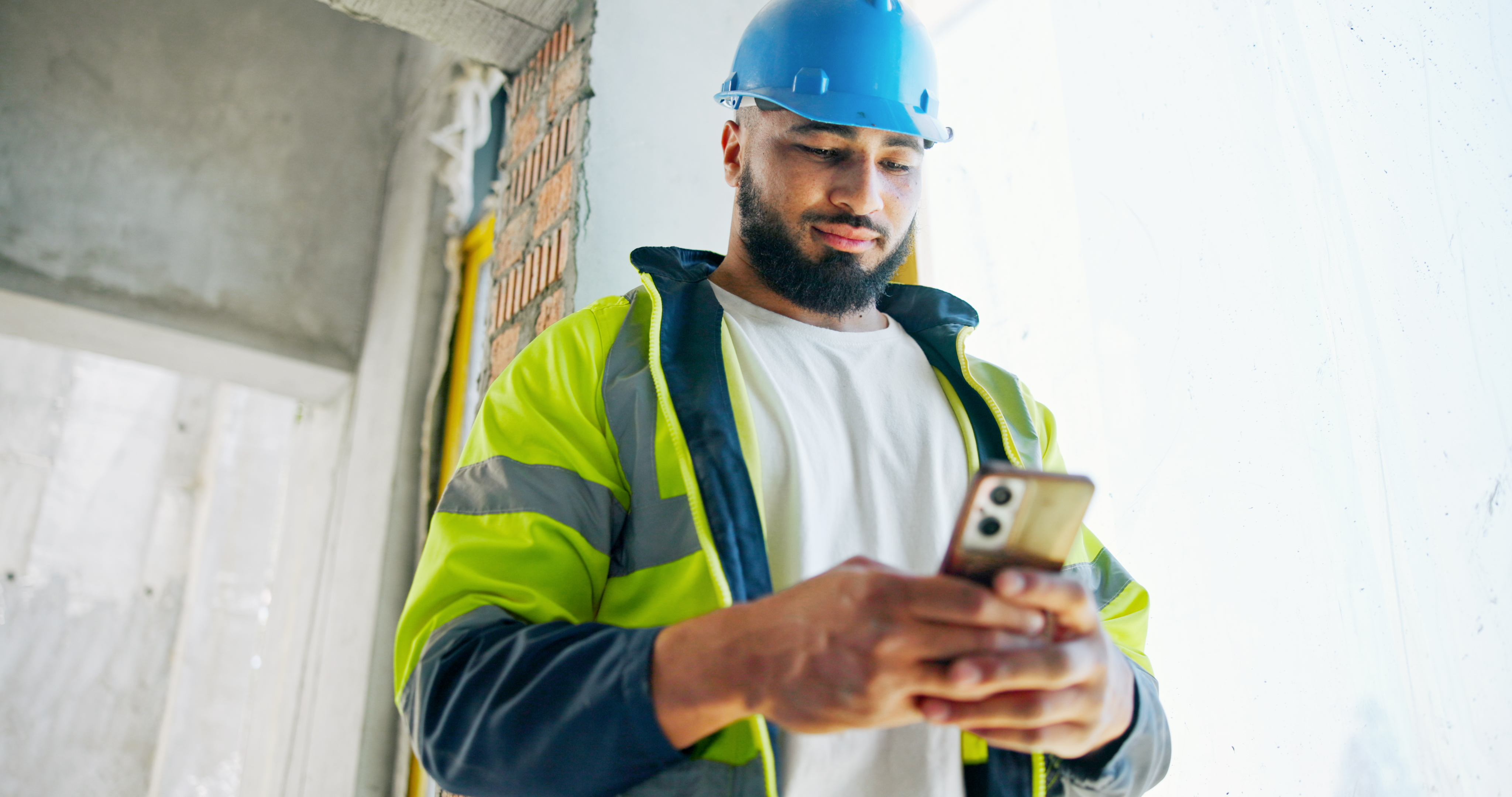 Man looking down at his phone, wearing hi-vis on a construction site