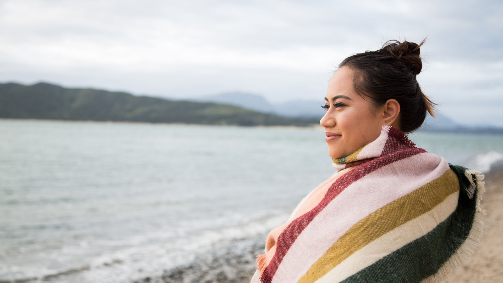 A Māori woman standing on the beach in the Hokianga harbour looking out to sea.