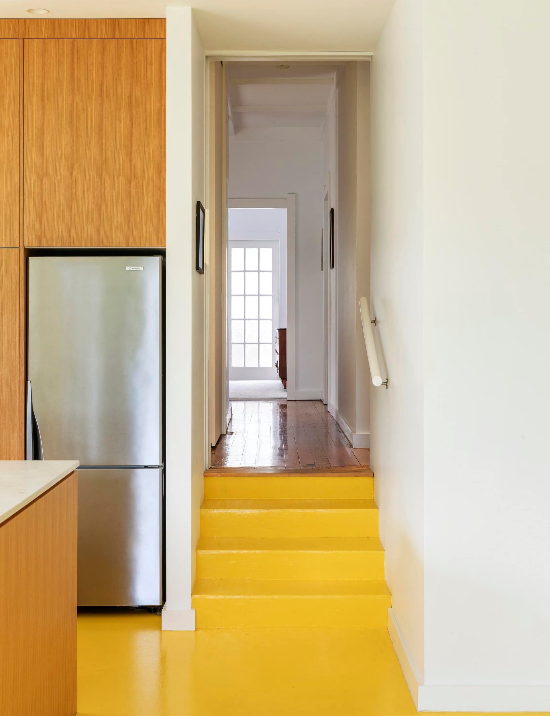 Hallway that connects to a small set of yellow stairs to the yellow kitchen floor