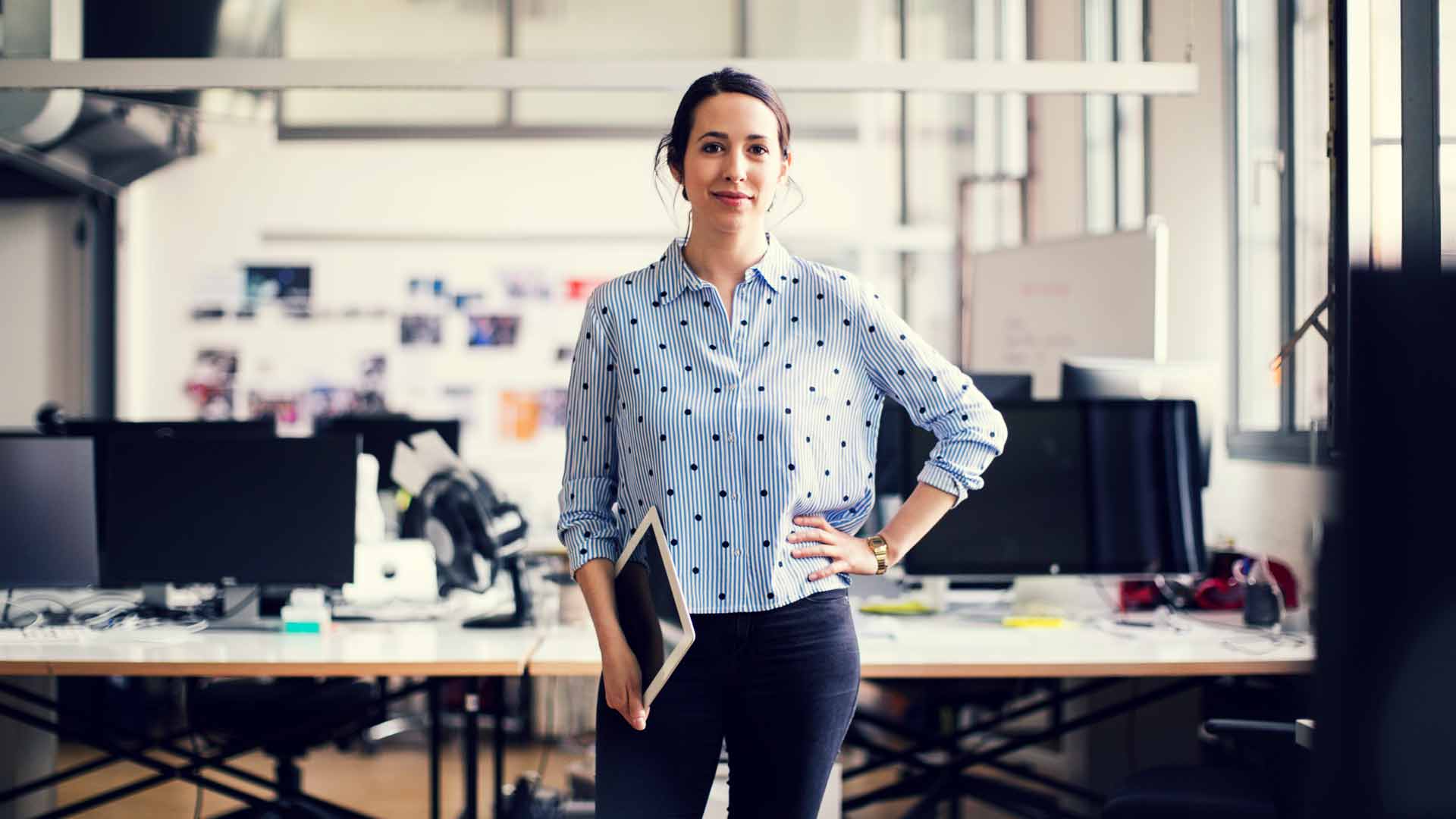 Woman dressed in a smart shirt and jeans, standing in an office.