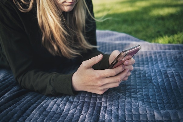 A woman lying on a blanket in the park using her phone to place feedback on a Trade Me sale.