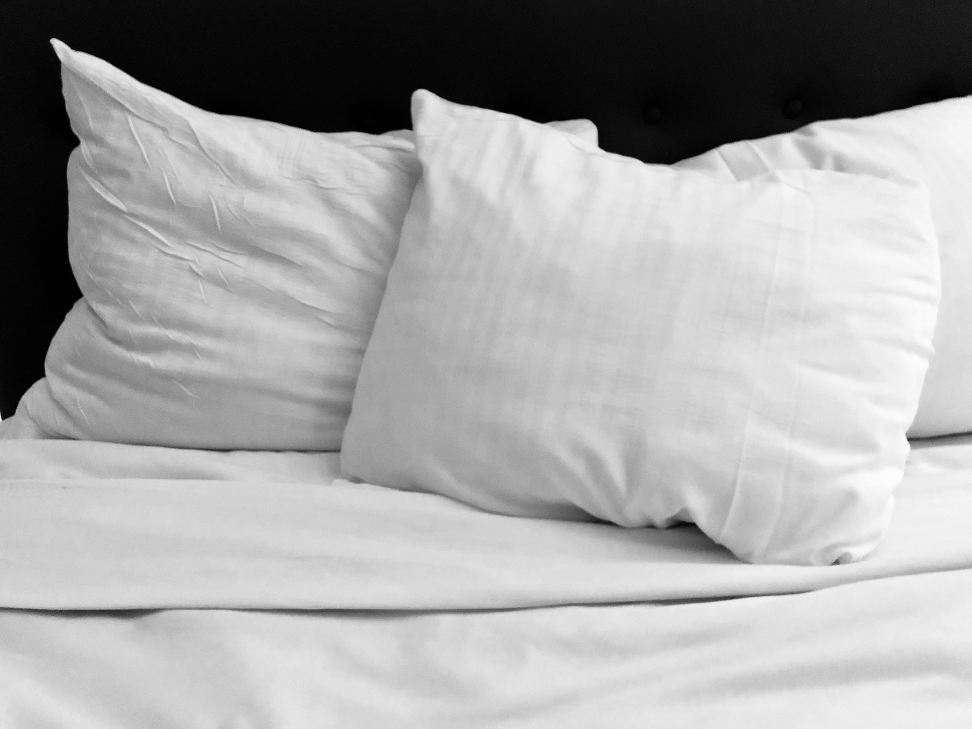 A set of white pillows on a bed with white sheets, in front of a black wall