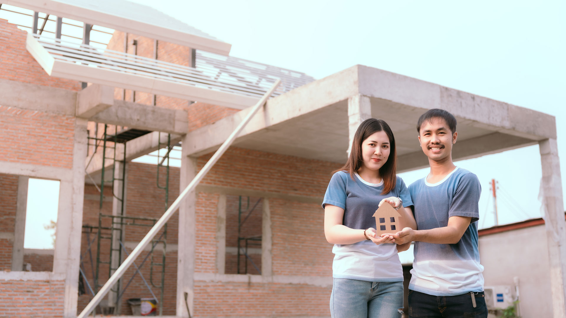 A couple who have bought an off plan home in NZ standing outside the property while it's under construction.