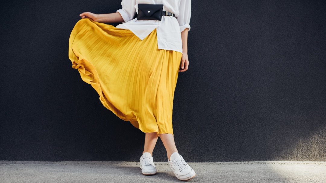 Woman walking outside holding up one side of a long yellow secondhand skirt she has bought online.