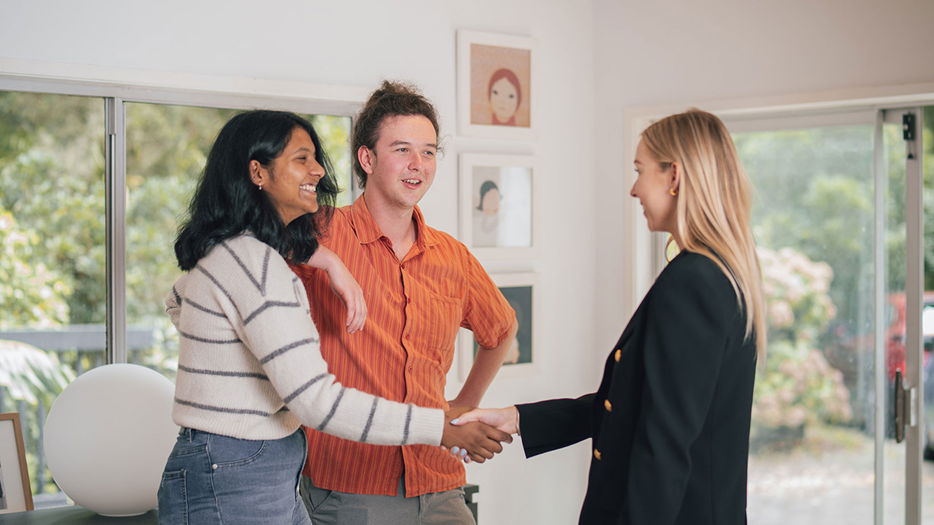 Couple shaking hands with a real estate agent in the living room of a home.