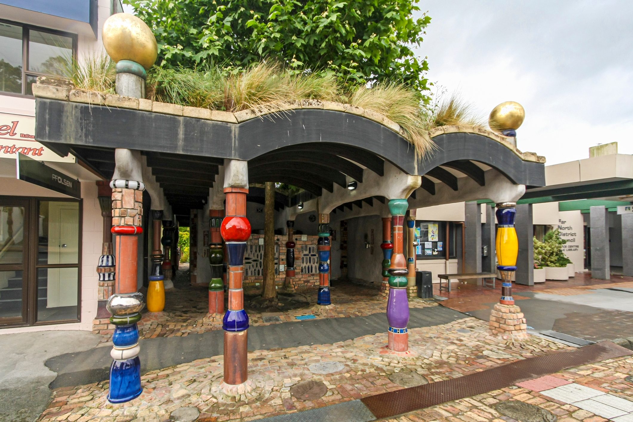 Multicoloured columns outside of a public toilet. The public toilet is covered in multicoloured tiles. 