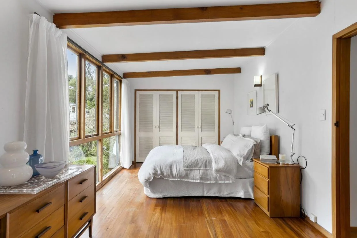 A spacious bedroom looks out to bush.
