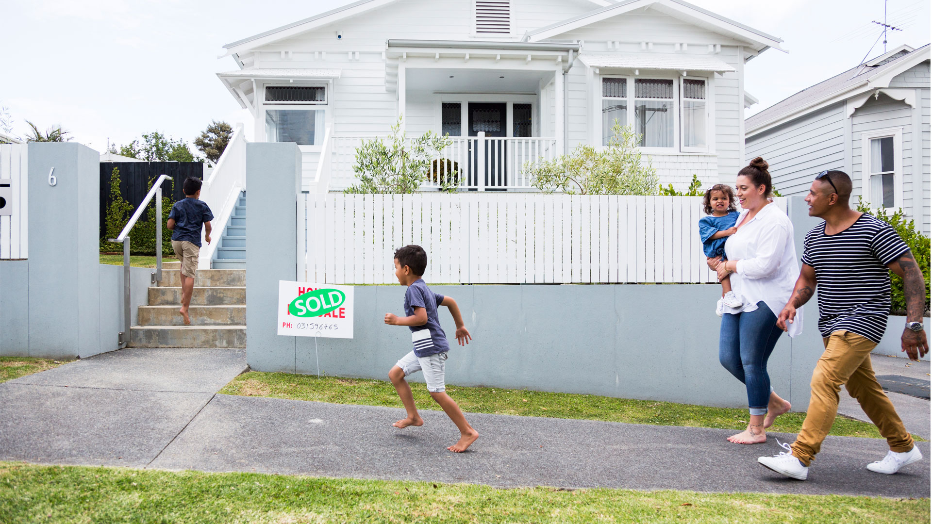 Family running up to their newly purchased home in Auckland with a for sale sign outside it.