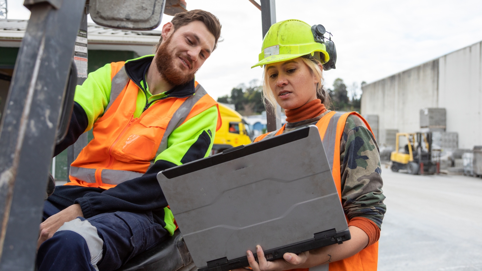 Man on forklift speaking to lady with laptop in high vis. 