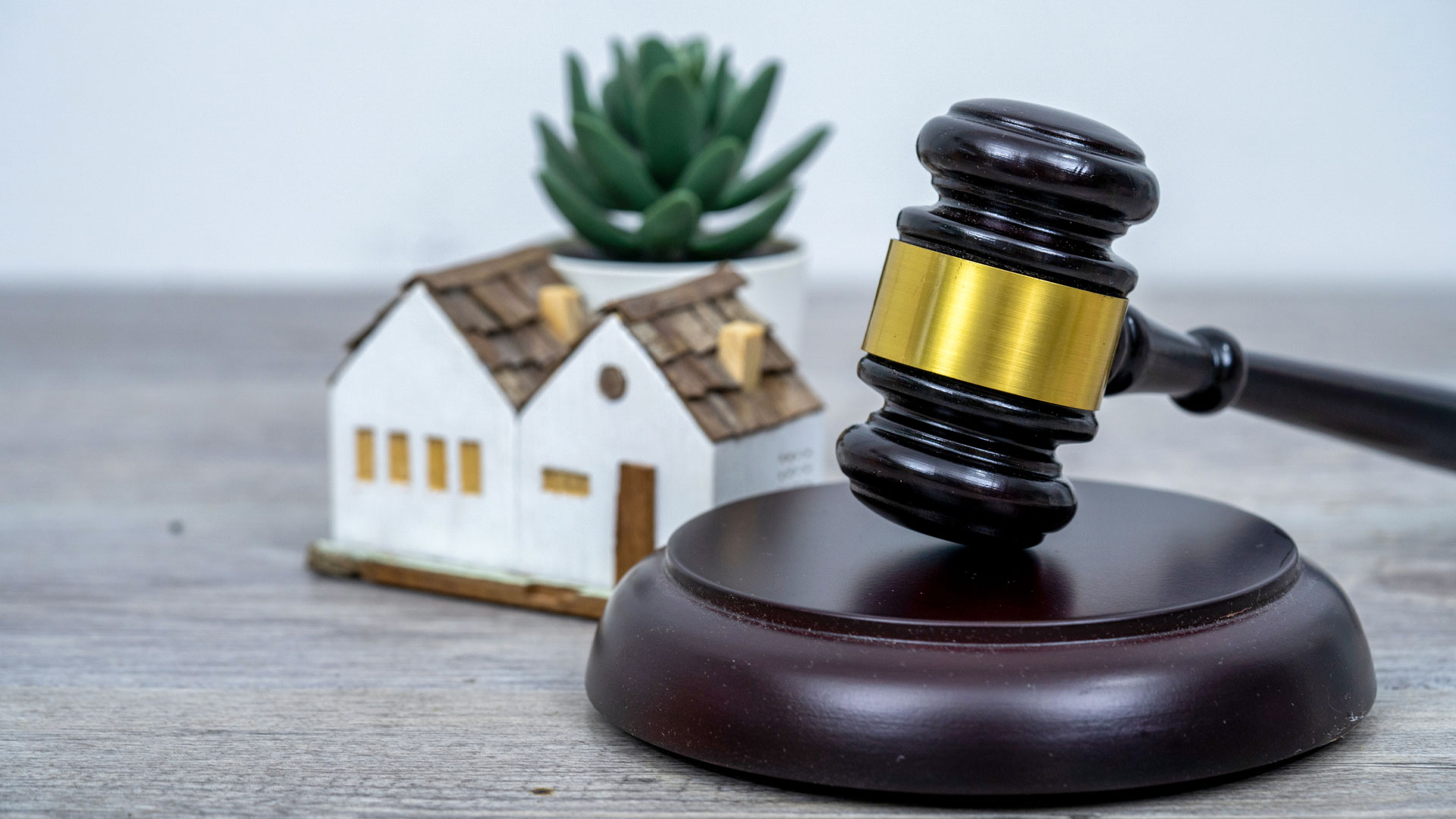 An auction gavel on a desk next to small model house.