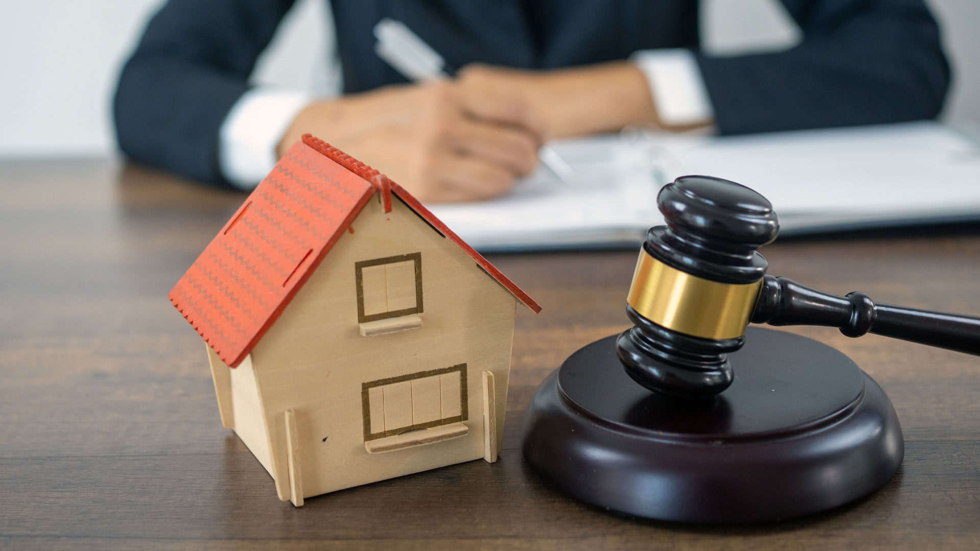 An image of an auction desk with a miniature home next to an auction hammer.