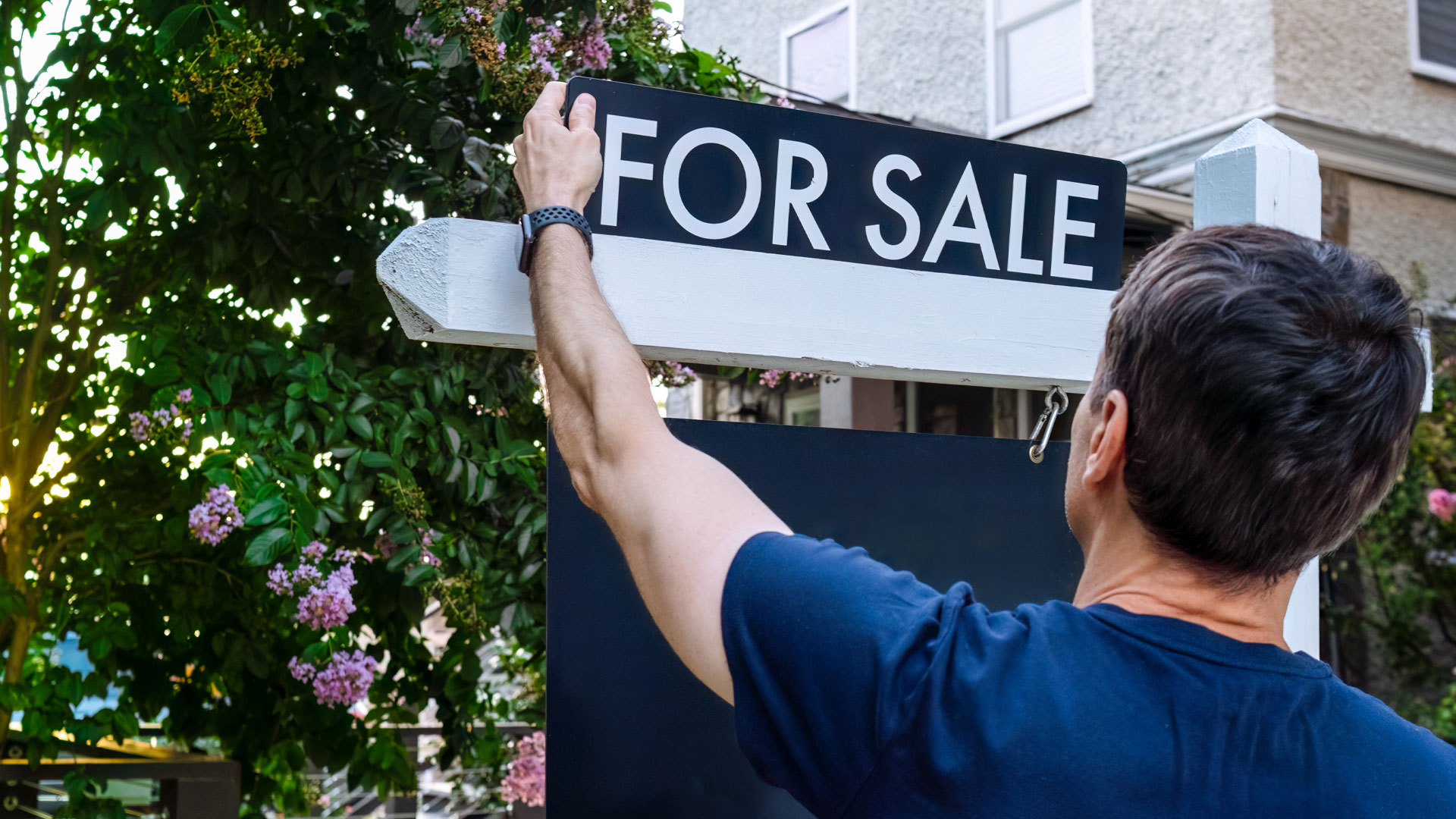 A man putting up a for sale sign in front of his house in NZ.