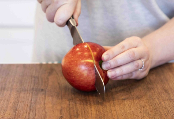 One hand holding an apple while the other hand is slicing the apple in half