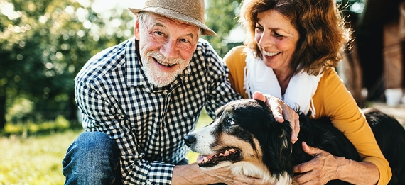 Older man and woman petting their dog outside