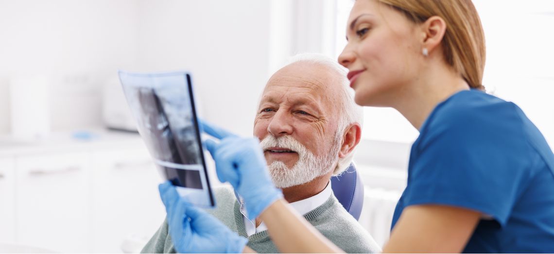 Elderly man in a dentist office reviewing x-ray with physician