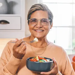 Older  woman eating a salad in the kitchen.