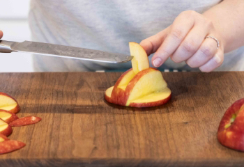 A hand holding the neck of the swan in the opening of the side half of the apple