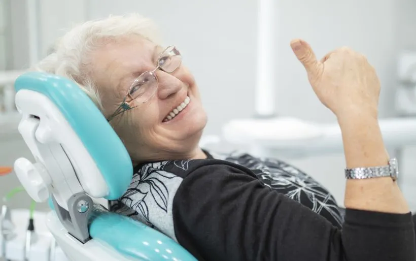 Older dental patient in dental chair smiling and giving thumbs up