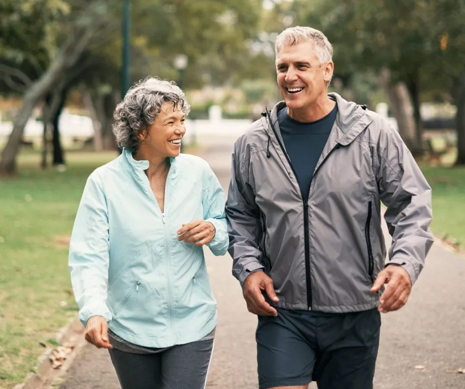 Older man and woman couple with gray hair smiling and walking outside in a park with trees