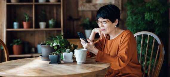 Older woman looking at her phone seated at table surrounded by plants