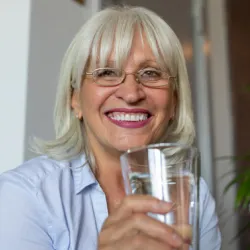 Older woman smiling holding a glass of water. 