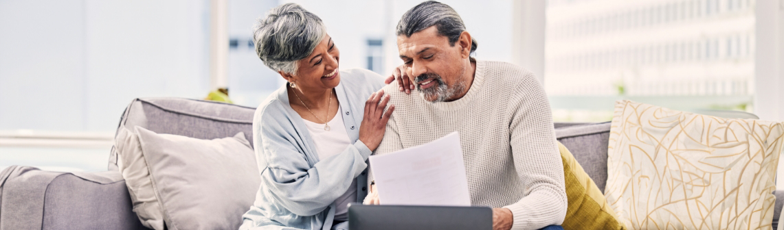 Older man and woman sitting on a couch looking at papers