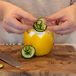 Image of the rolled cucumber peels in the shape of petals being placed in a yellow bell pepper