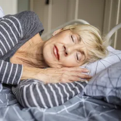 Older woman is sleeping in bed at home.