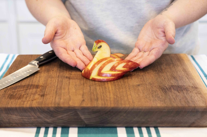 A person displaying the completed 'swan apple' on a cutting board