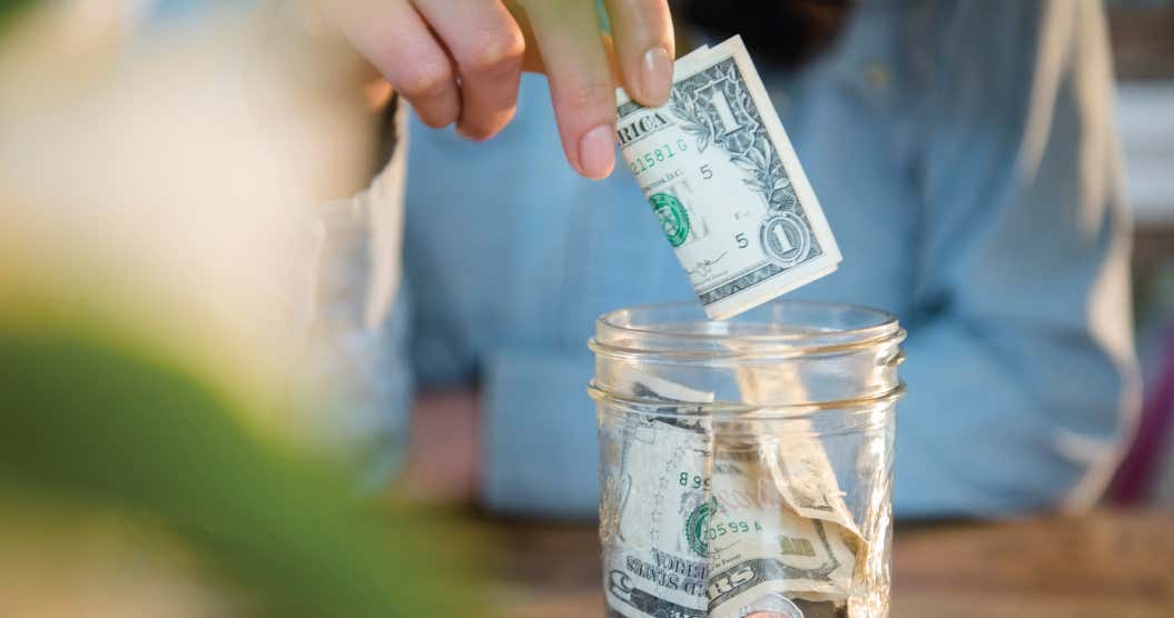 A hand putting money in a jar to build a savings