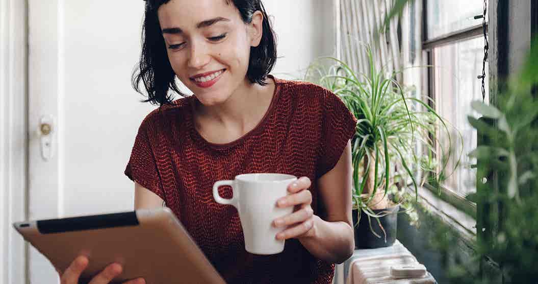 Woman holding a coffee and researching personal loans on her tablet