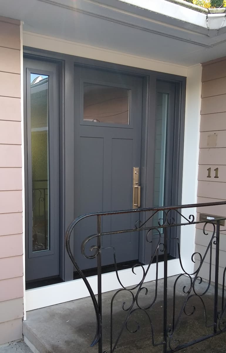 New black fiberglass entry door system with twin sidelights on a home with brown siding.