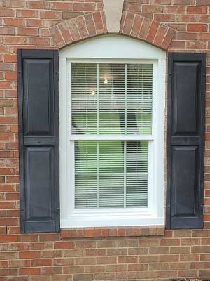 Post-installation shot of white vinyl windows with black shutters on brick Brentwood, TN, home