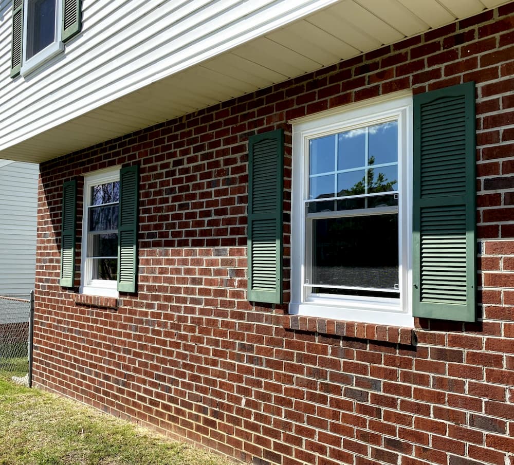 Two white double-hung windows on a red brick home