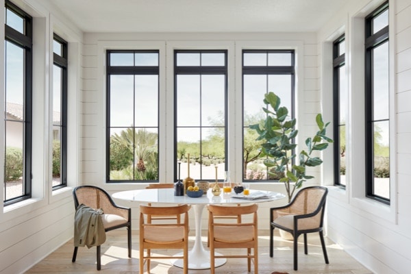 Black framed windows in wall of white shiplap above modern eclectic dining table